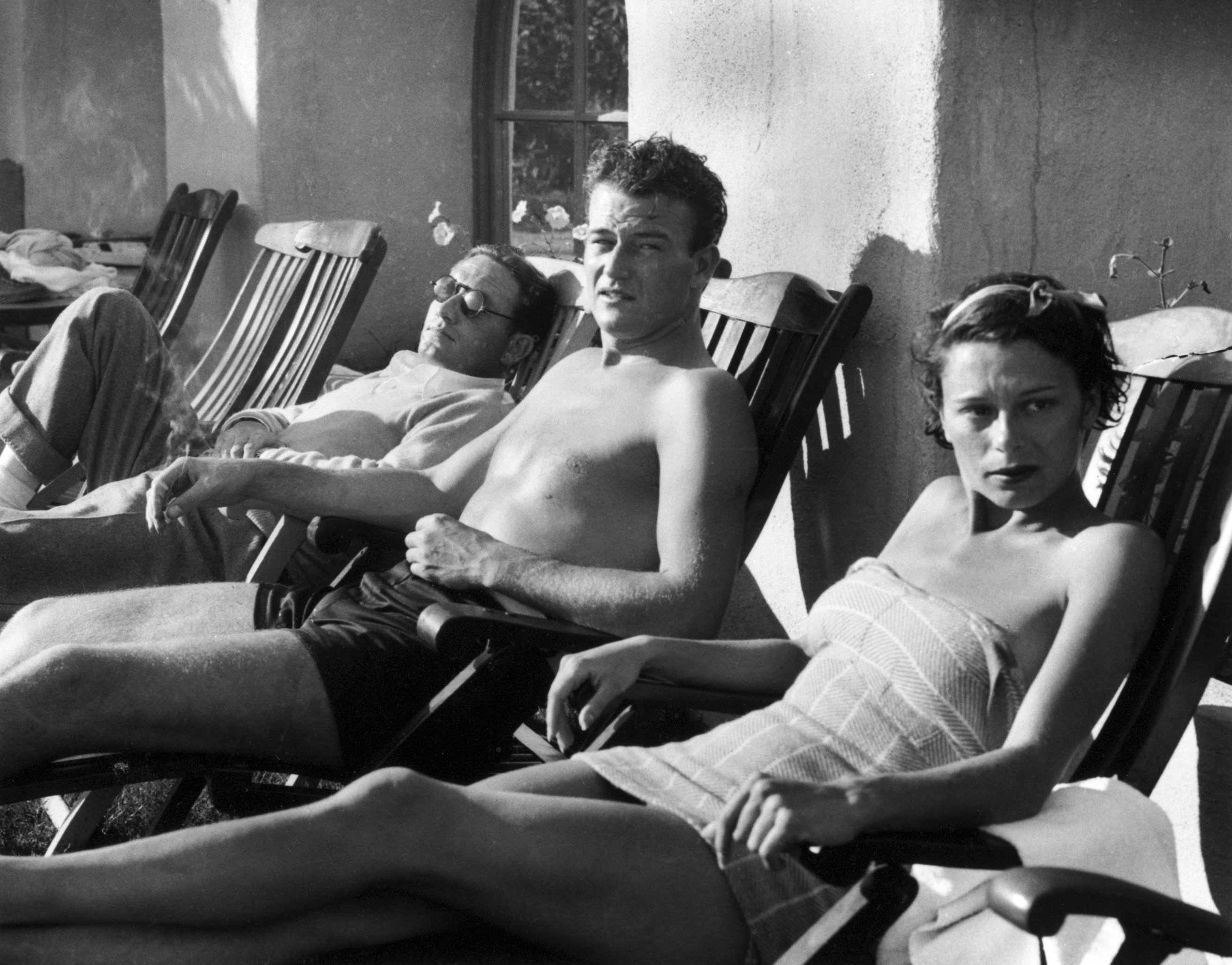 Spencer Tracy reclines in a deck chair next to John Wayne, and his wife, Josephine Wayne. The three relax at El Mirador in Palm Springs, California, on January 29, 1934.| Source: Getty Images